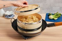 a person lifting the lid off a steamer basket with dumplings inside