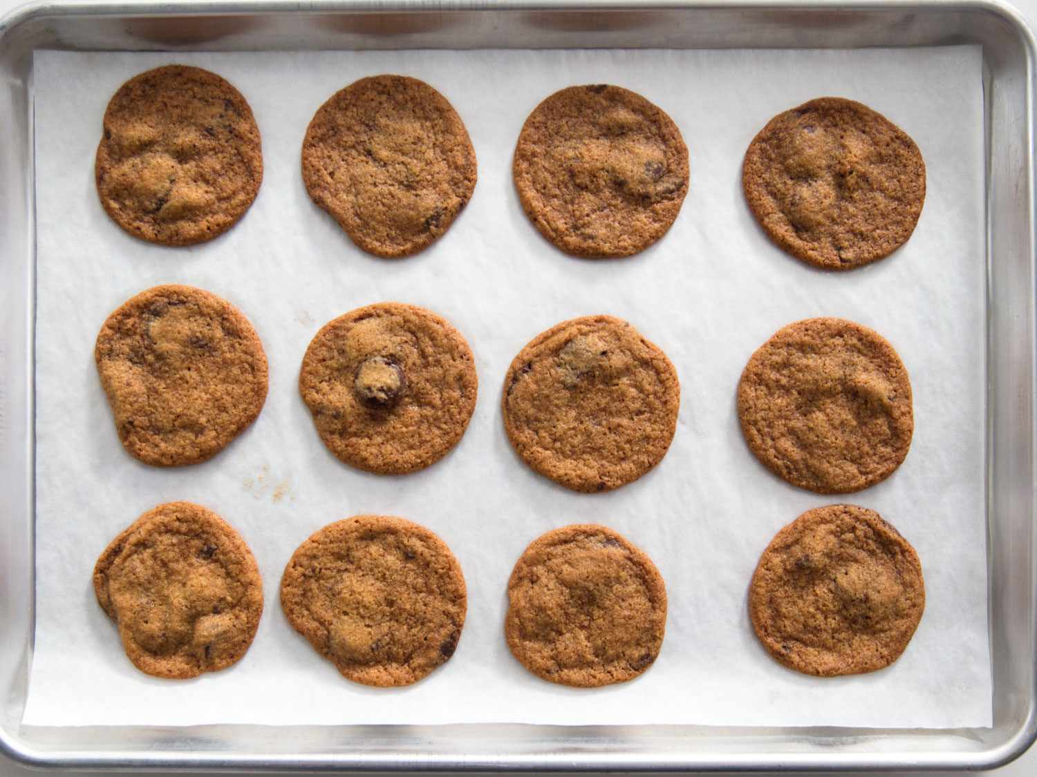 Overhead shot of thin and crispy Tate's-style chocolate chip cookies on a parchment-lined baking sheet.