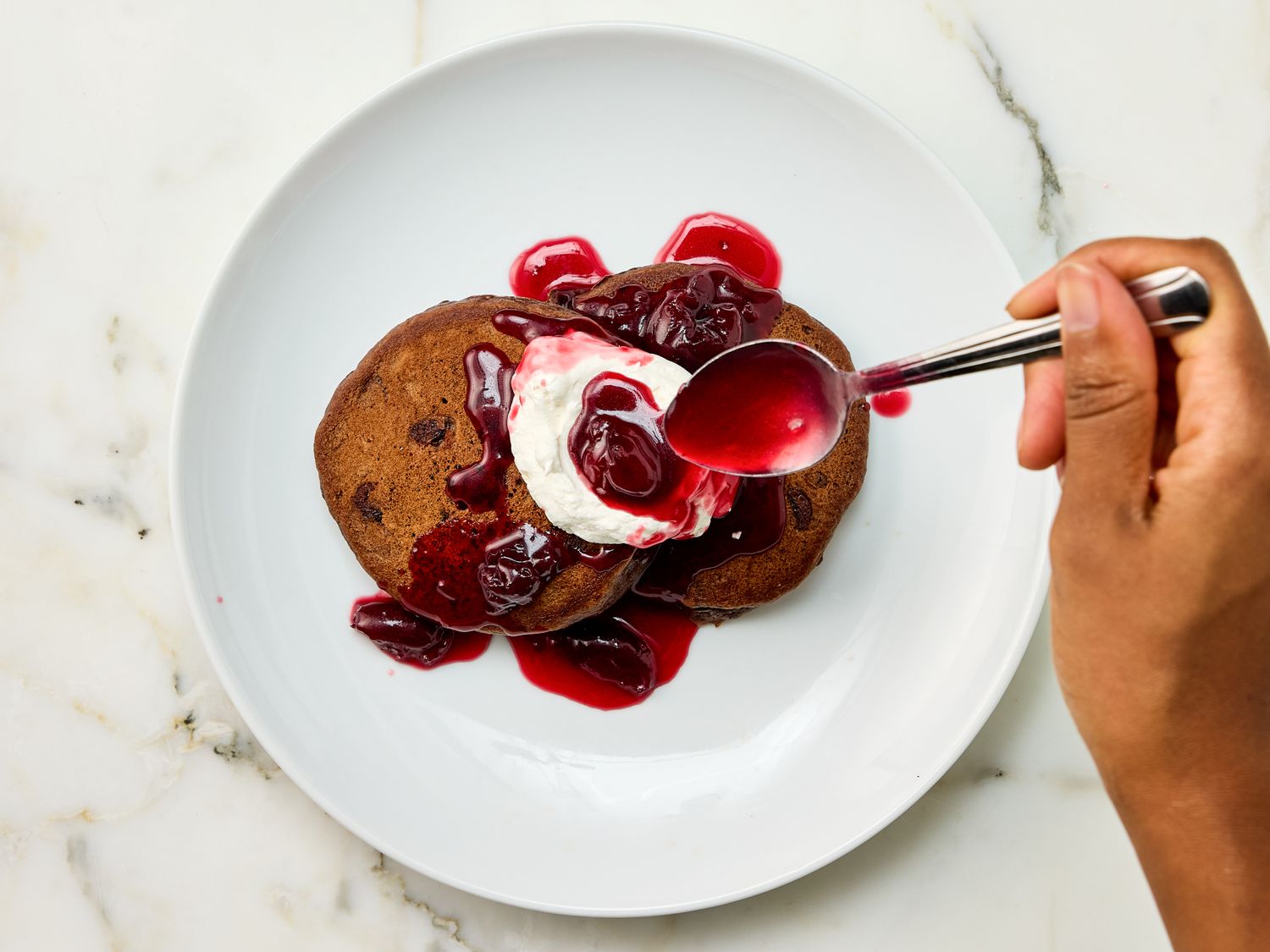 A hand spooning syrup over pancakes on a plate