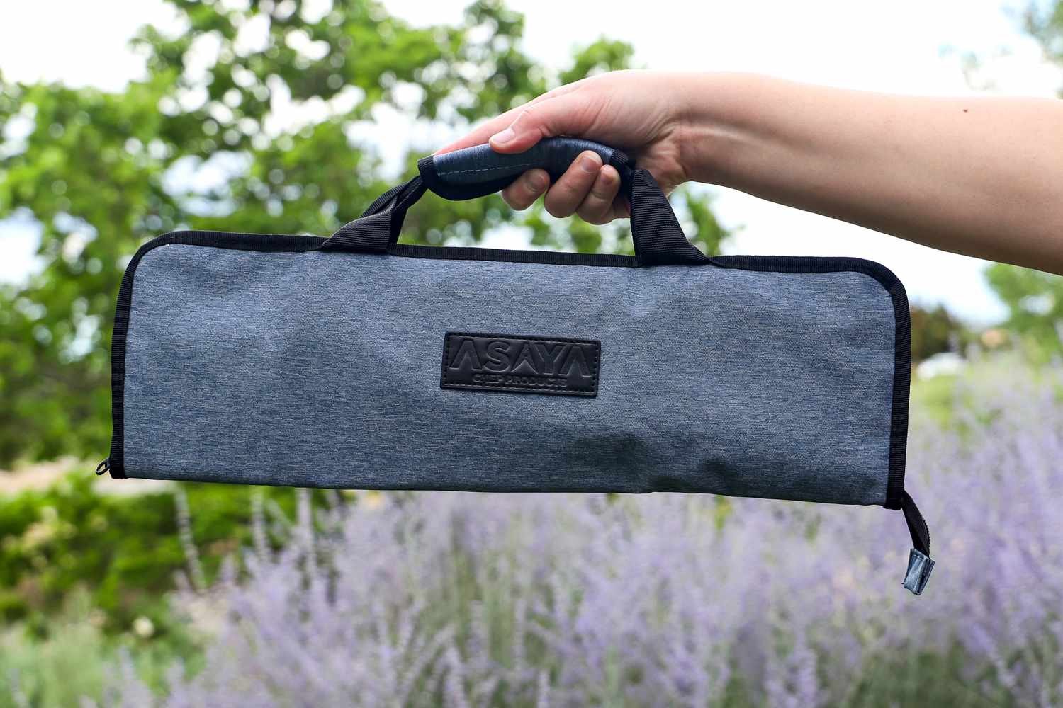 A hand holding a Asaya Chef Knife Roll Bag with the logo Asaya Chef Products visible on it