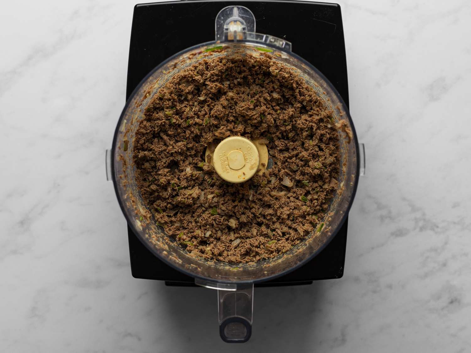 Half of the beef, half of the remaining bell pepper, and half of the remaining onion finely chopped inside a food processor bowl.