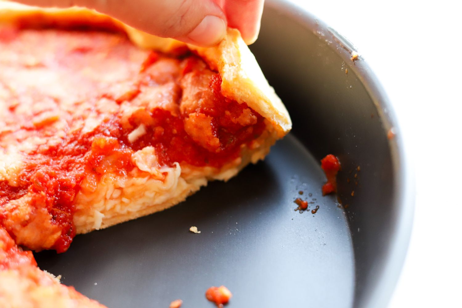 A person pulling a slice of pizza from the LloydPans Chicago Style Deep Dish Pizza Pan