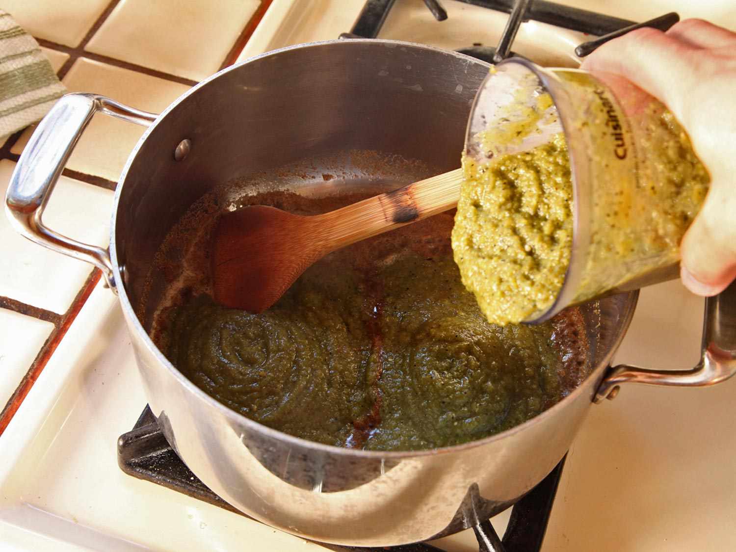 Adding chile purèe into a stock pot containing bloomed spices.