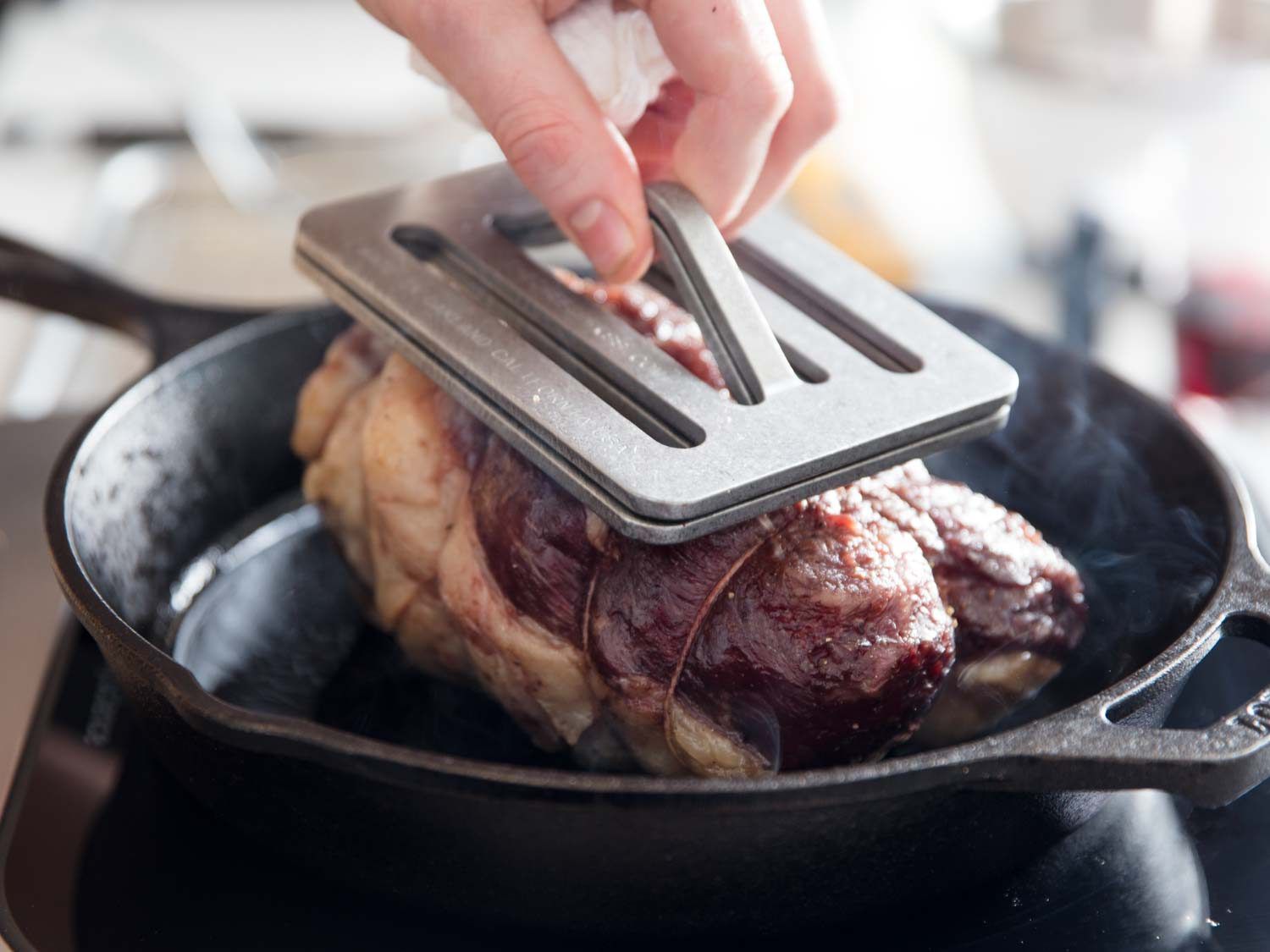 Beef roast browning in pan under a metal cooking weight.
