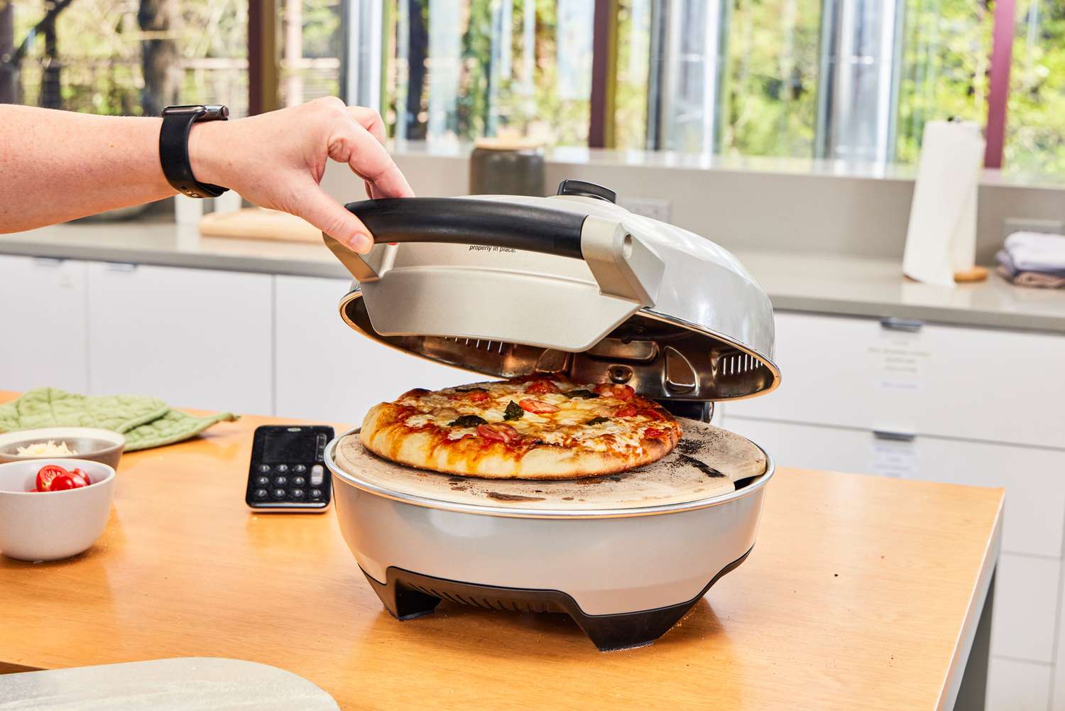 A person opening the lid of the Breville indoor pizza maker with a pizza inside