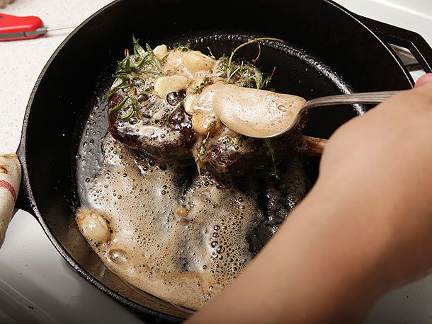 Basting butter over bison steak, garlic, and herbs in skillet.