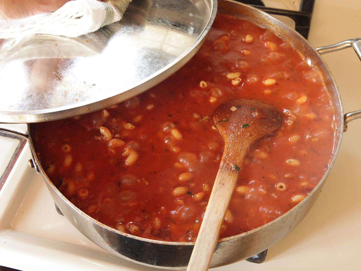 Shot of the sauté pan with the lid cracked and a wooden spoon stirring the contents.