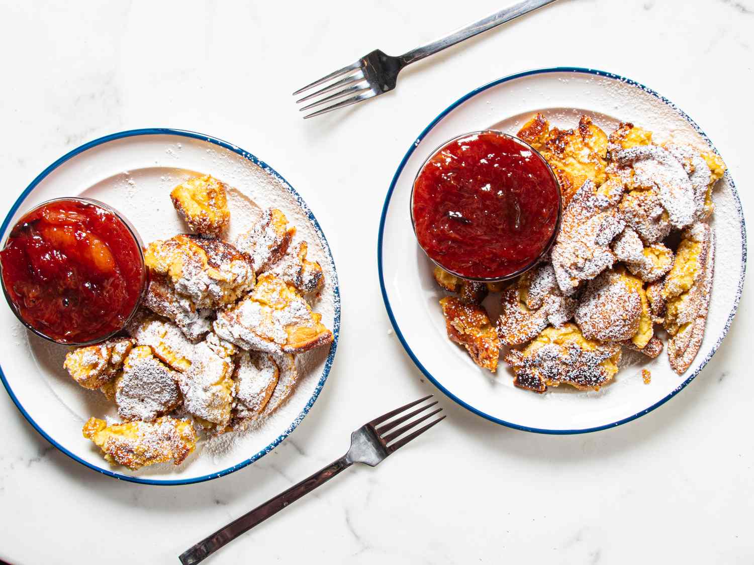 Two plates of Kaiserschmarrn with bowls of fruit compote on a table accompanied by forks