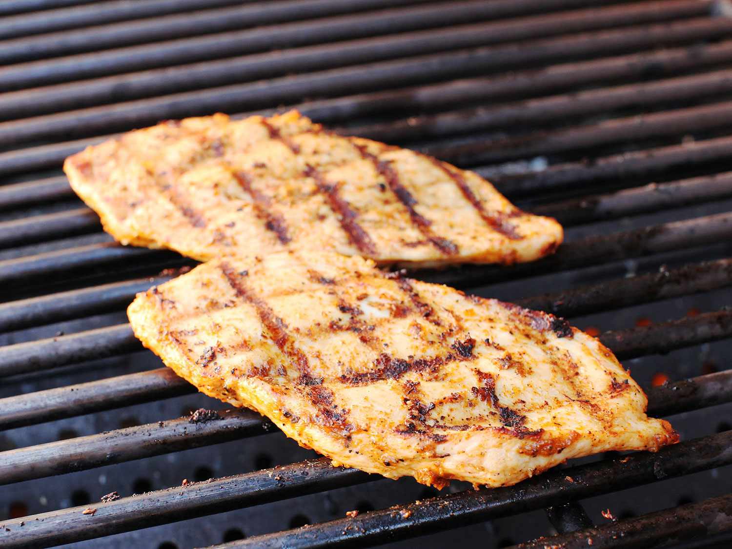 Two chicken cutlets resting on a grill grate with distinct charred marks. 