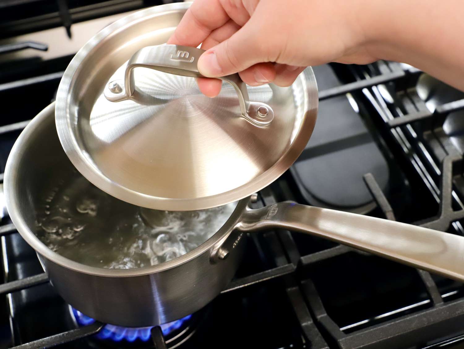 Person lifting lid from Made In Stainless Clad Saucepan with boiling water