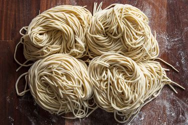 Freshly cut homemade ramen noodles in four nests on a flour-dusted wood surface.
