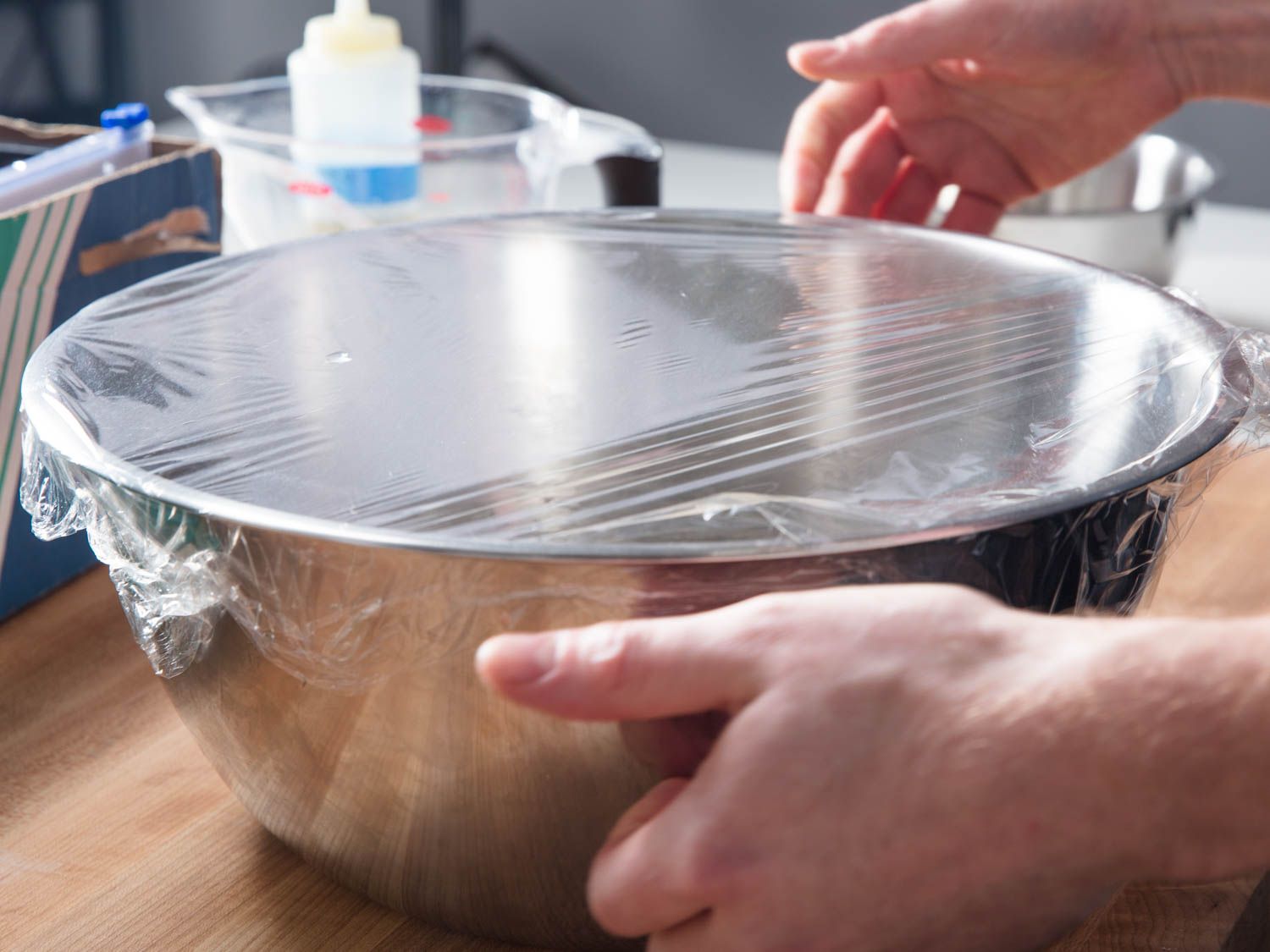 Covering large metal bowl filled with plastic wrap.