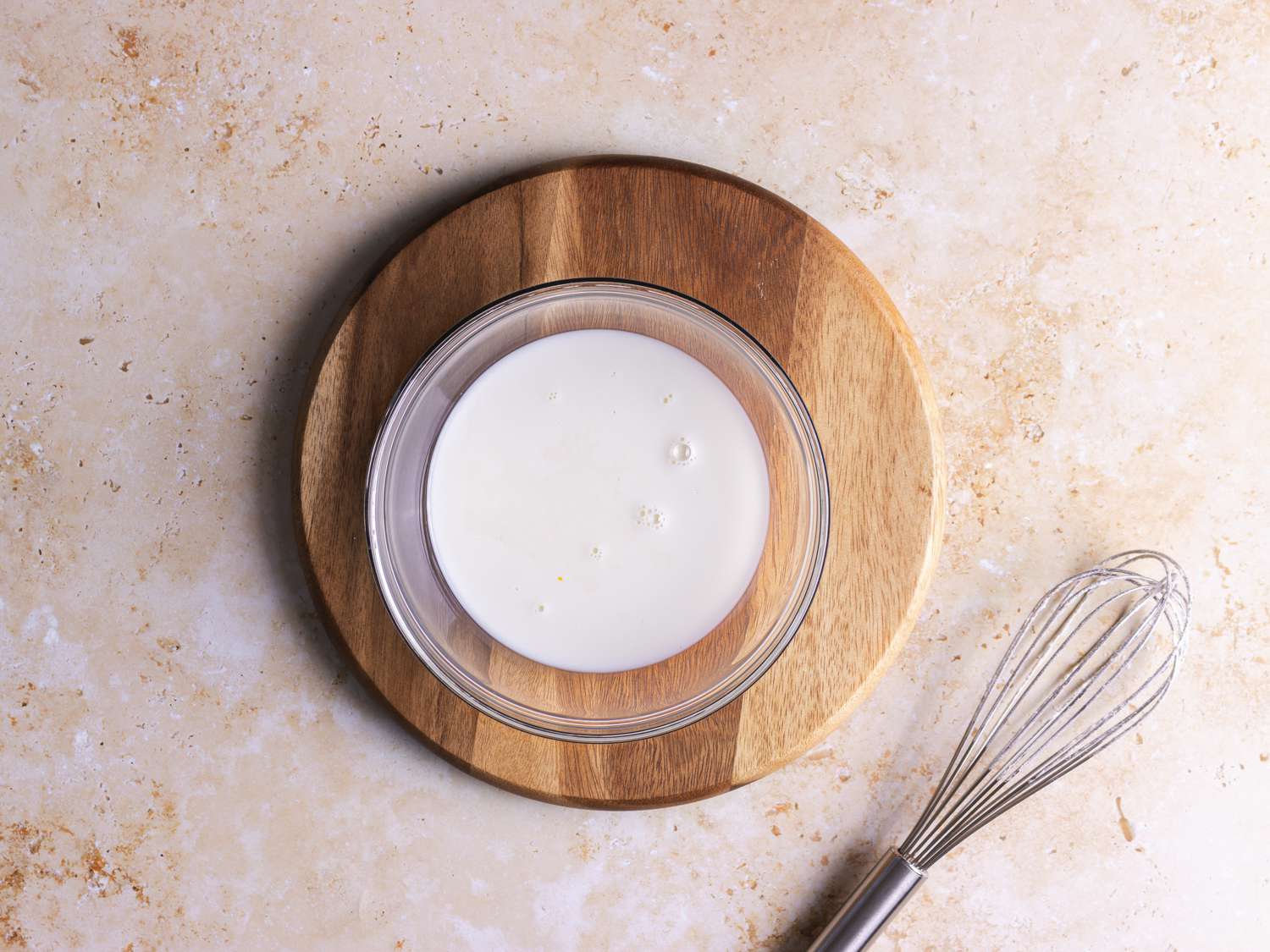 Milk and vanilla in a bowl on a wooden plate with a whisk nearby