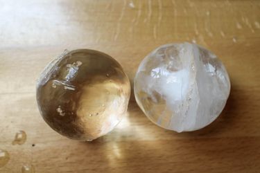 A clear sphere of ice to the left of a cloudy sphere of ice. 