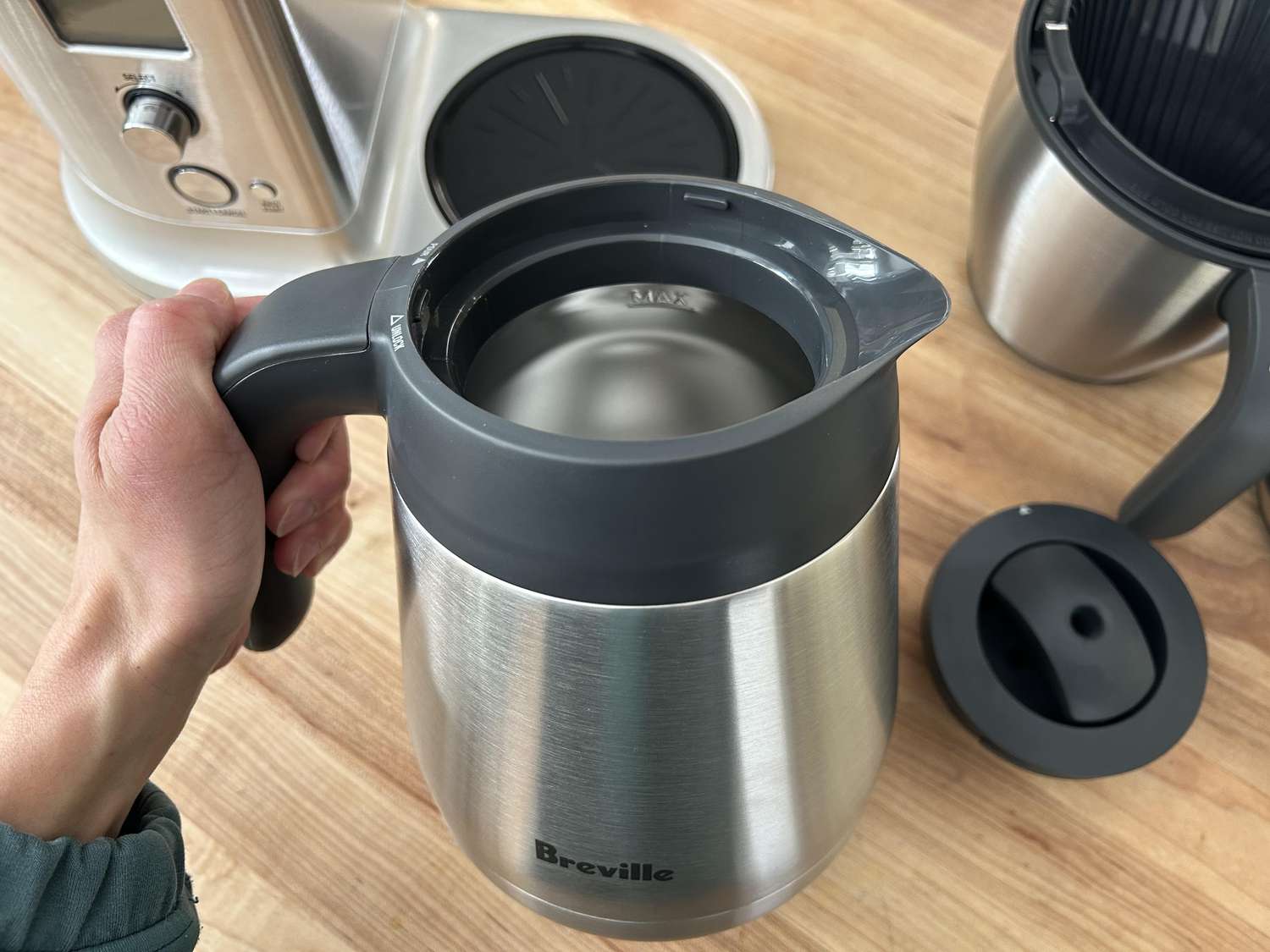 A hand holding the Breville thermal carafe in front of the coffee maker.