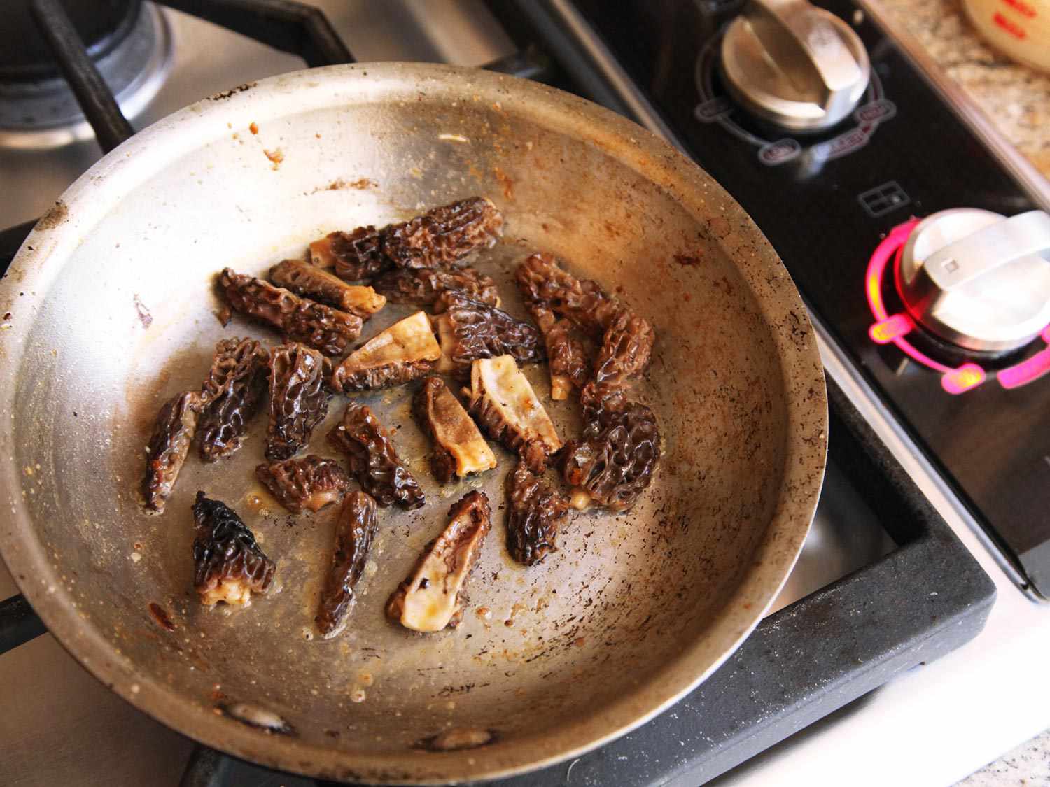 Cleaned, cut up morel mushrooms browning in a stainless steel pan.