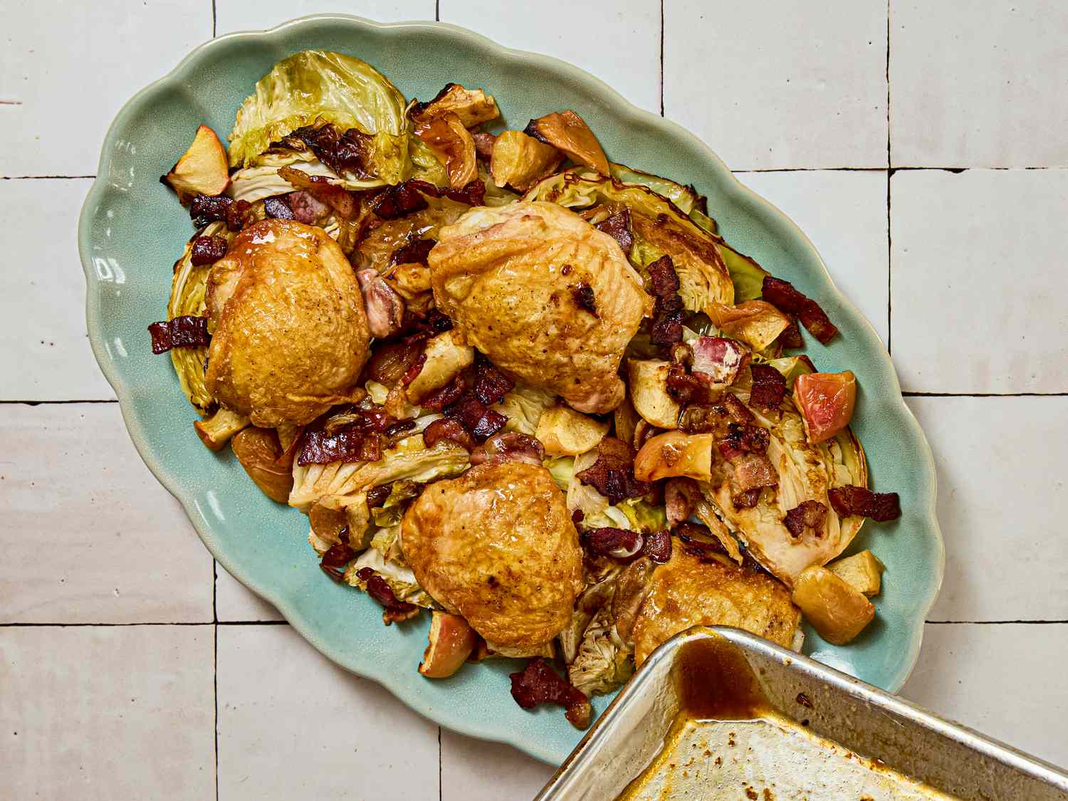 Sheet pan of cooked chicken thighs with bacon and apple pieces on a platter