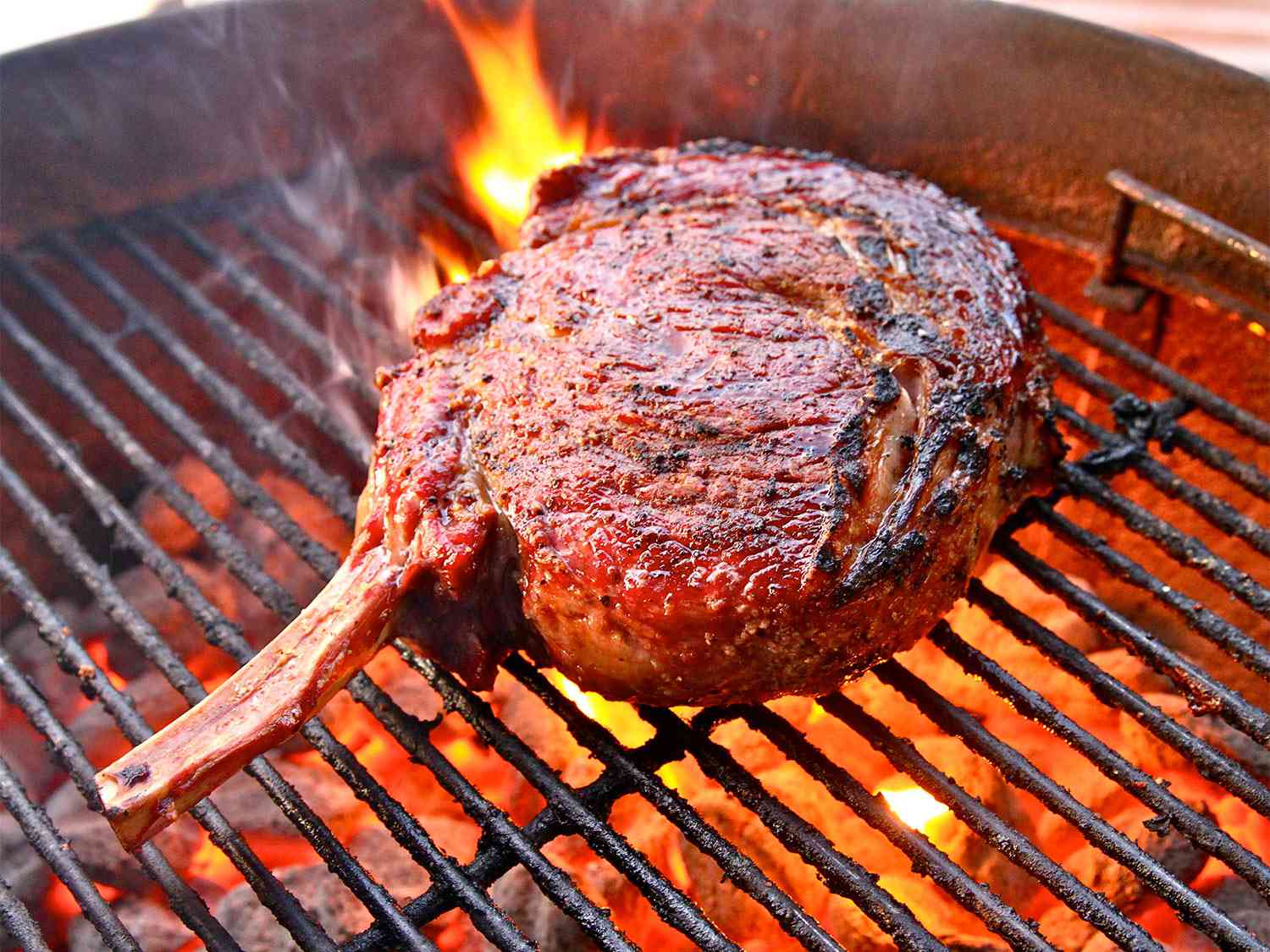 A cowboy steak (bone-in ribeye) cooking on a grill.