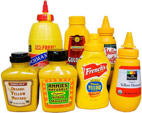 An assortment of seven bottles of yellow mustard. 