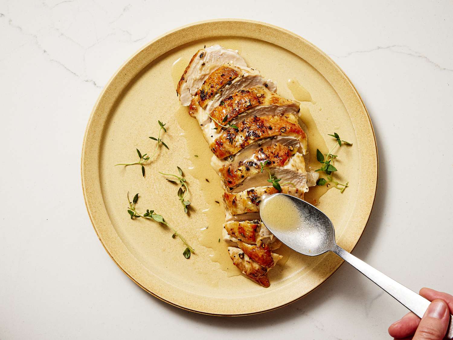 Sliced chicken breast with lemon juice being spooned onto it on a yellow toned plate 