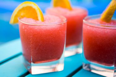 a profile view of a rocks glass filled with red frozen negroni, garnished with an orange wedge