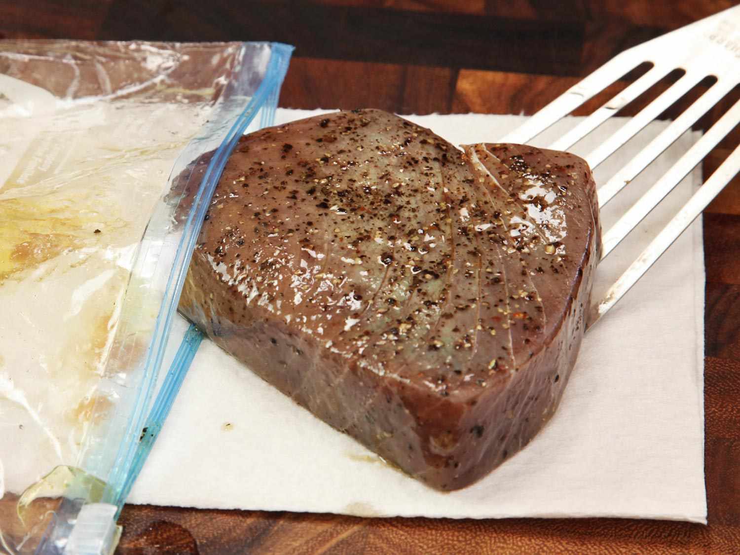 A tuna steak being removed from the zip-lock bag it was cooked in and placed on a paper towel.