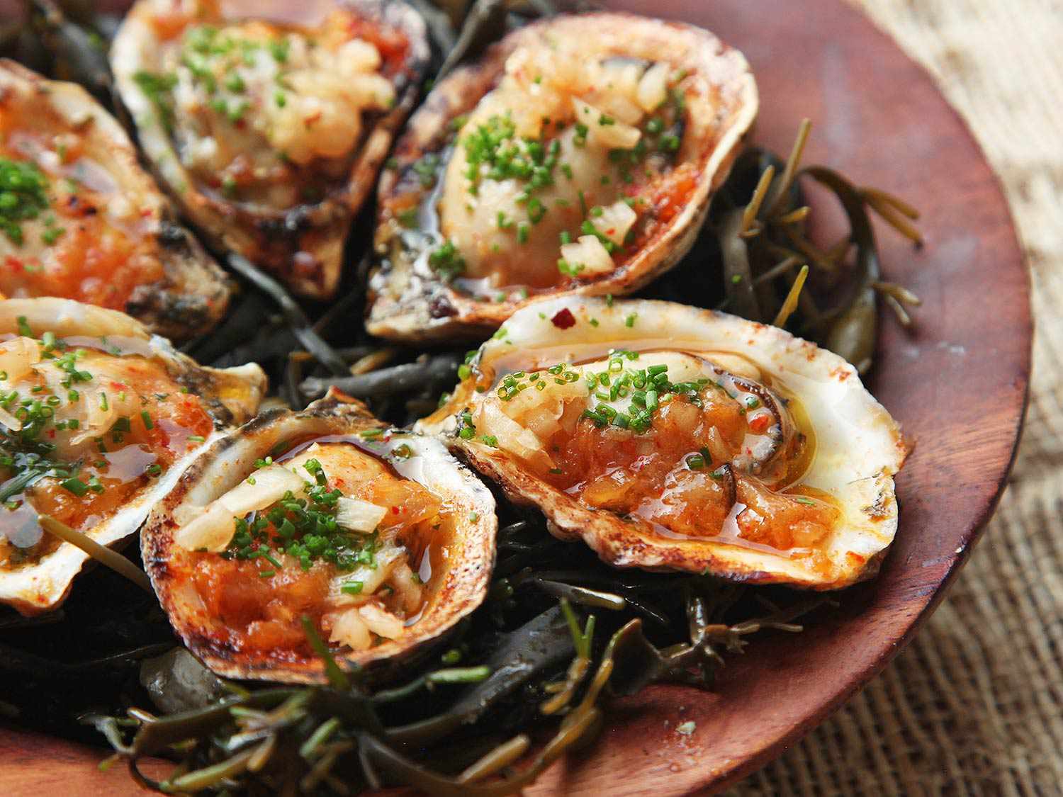 Platter of grilled oysters with kimchi butter on a bed of seaweed.
