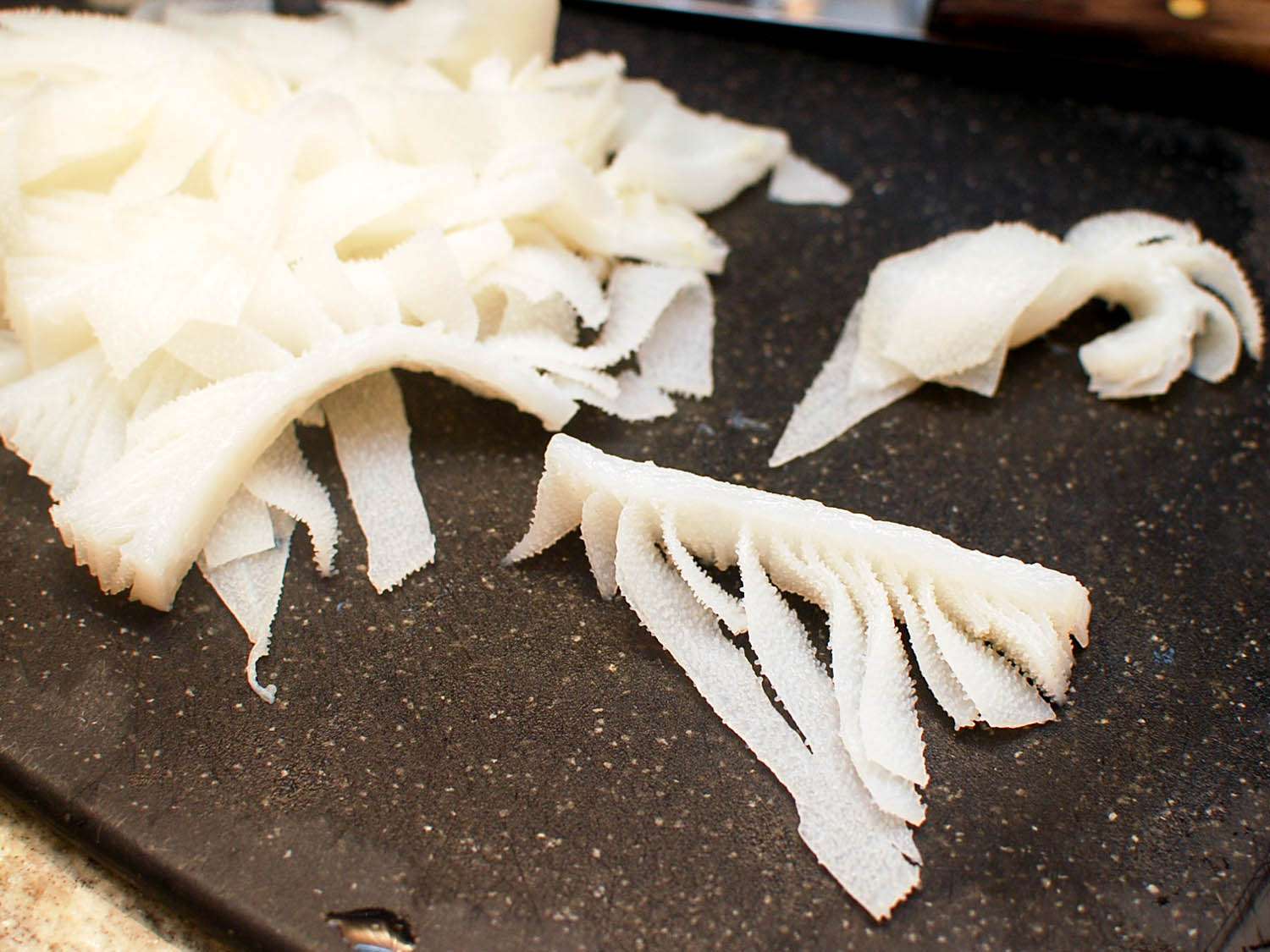 The tripe is cut into bite-sized pieces on a black cutting board.