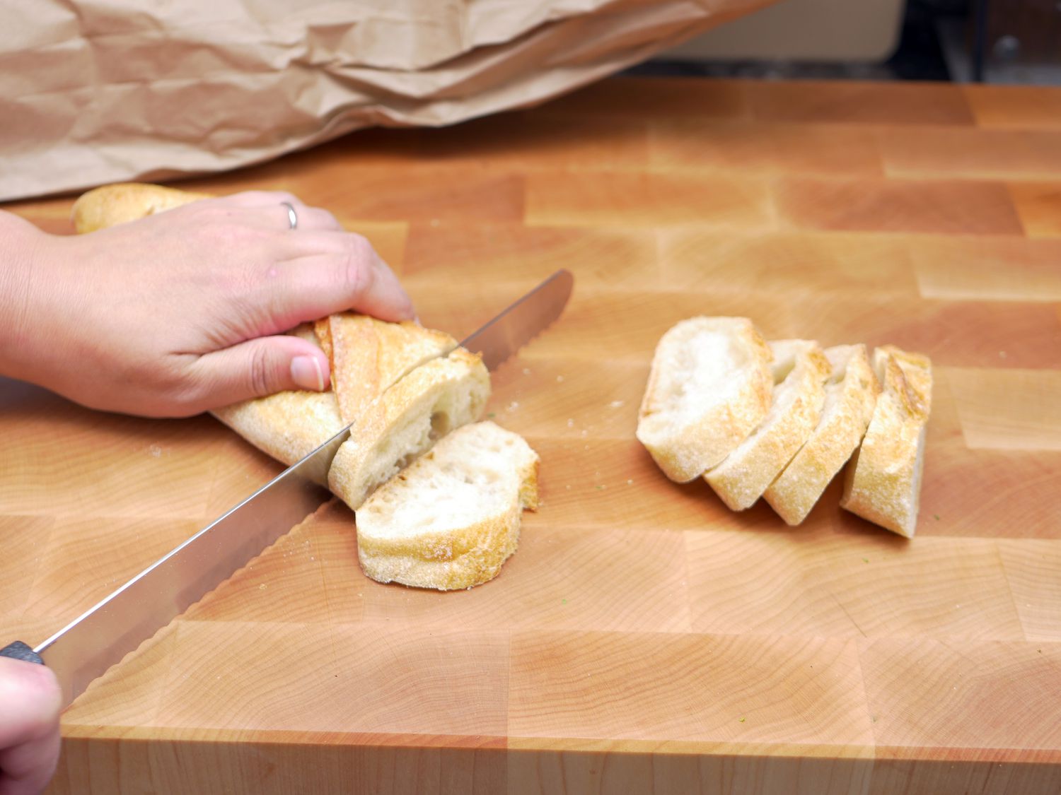 slicing a baguette with a bread knife on a wooden cutting board