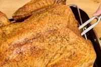 A person piercing a fully-cooked Grassland Beef Pasture Raised Turkey with a fork