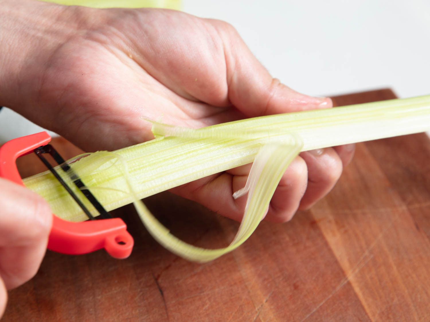 Hands peeling celery rib with y-peeler