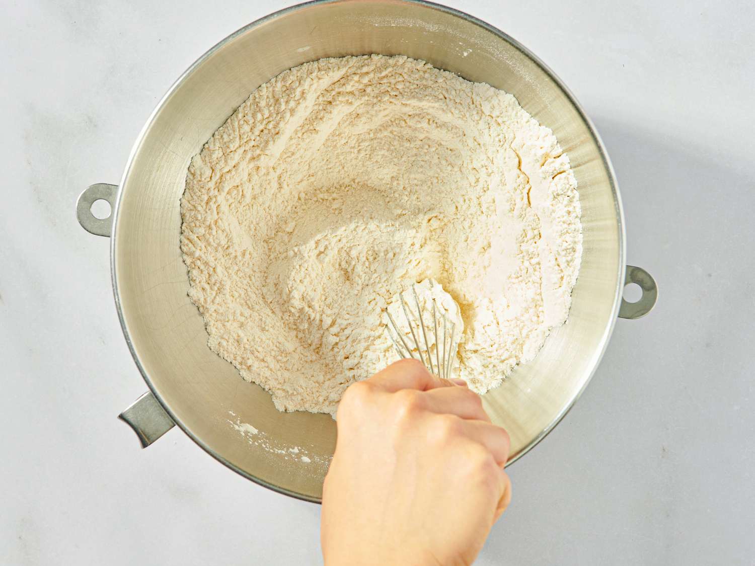 A hand whisking a bowl of flour mixture