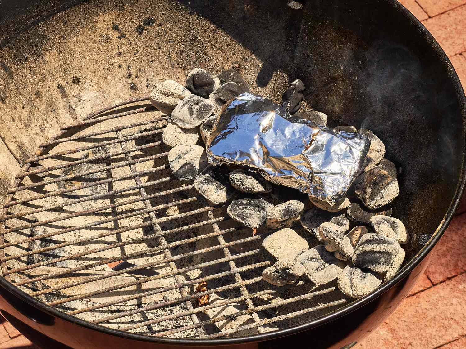 Corn wrapped in foil cooking on a barbecue grill with charcoal
