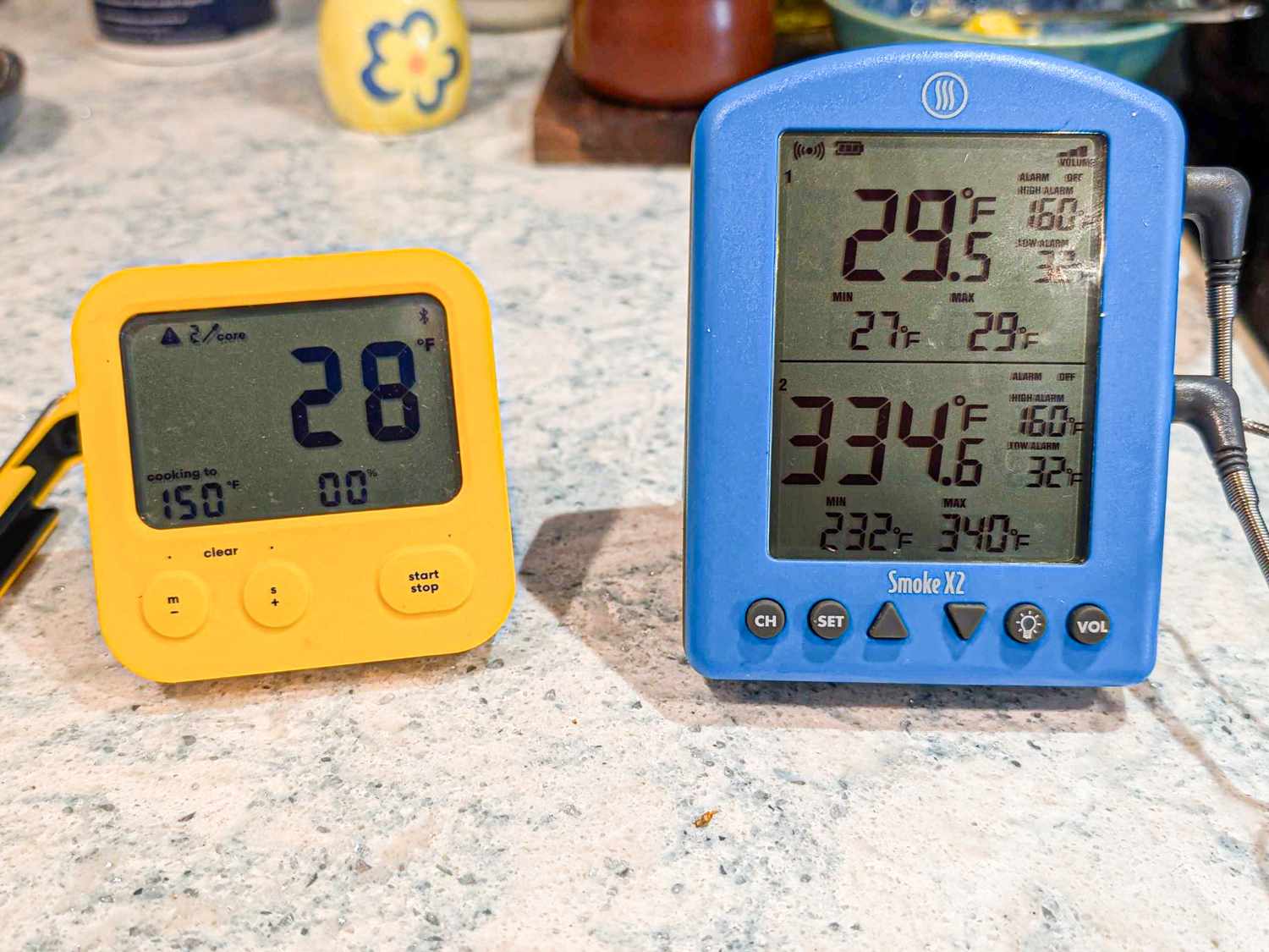 Two digital cooking thermometers displaying temperature readings placed on a countertop in a kitchen setting