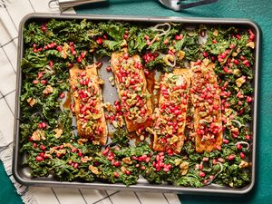 Salmon fillets topped with pomegranate seeds and greens on a baking sheet