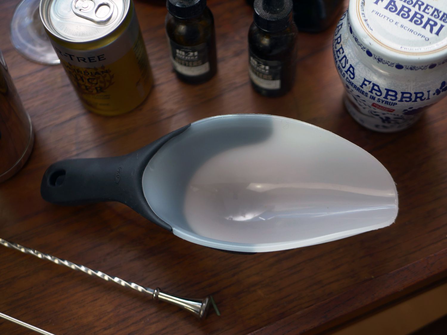 oxo ice scoop on a wooden bar cart with bitters, tonic, and other bar essentials
