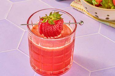 A glass of strawberry smash cocktail with a whole strawberry garnish