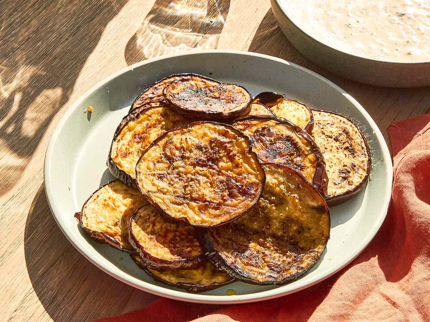 Plate of grilled eggplant slices served on a wooden table with side dishes