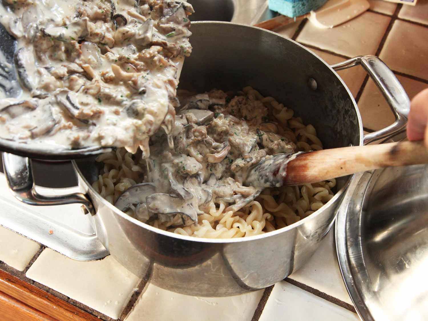 Transferring mushroom cream sauce from the skillet to the pot of pasta. 
