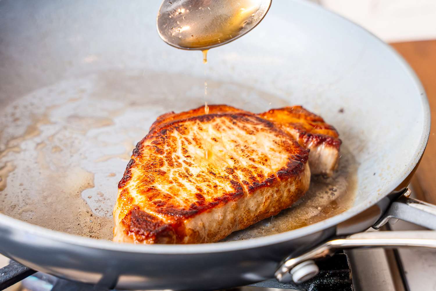 A spoon basting a pork chop with butter in the Greenpan Valencia Pro ceramic skillet.