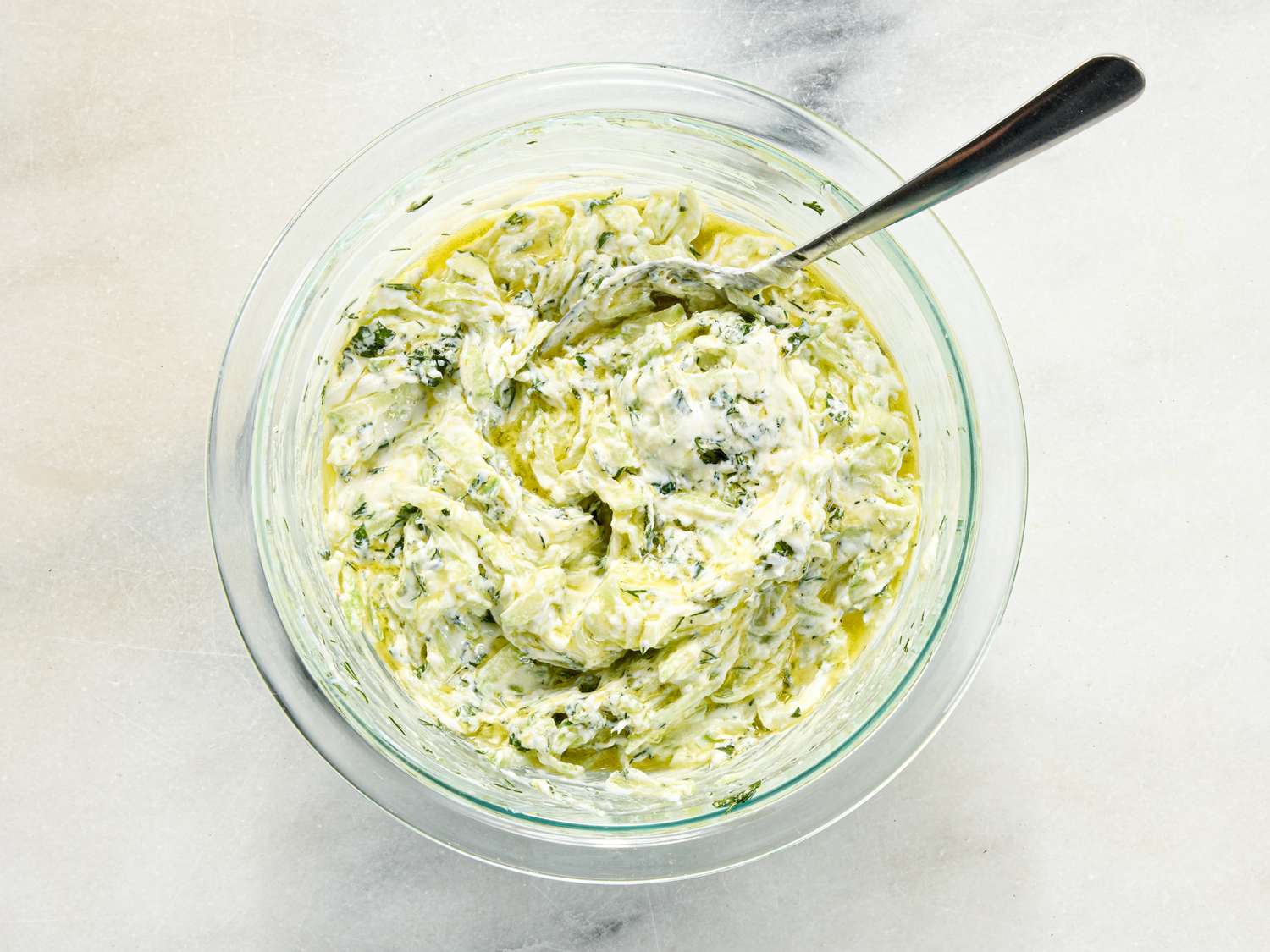 A bowl of Greek yogurt mixed with herbs and olive oil a spoon in the mixture