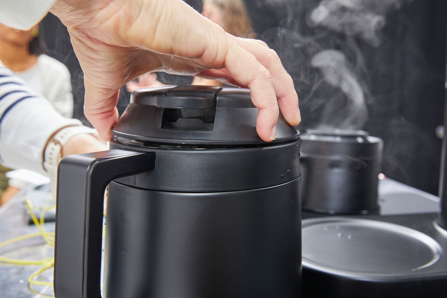 A hand unscrewing the lid on the Ratio Six Coffee Maker's carafe.