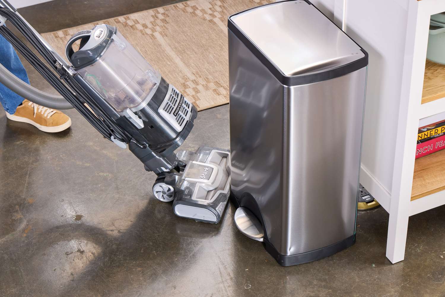 A person vacuums near the simplehuman 38-Liter Brushed Stainless Steel Steel Trash Can with Lid
