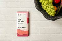 The Raaka Pink Sea Salt Dark Chocolate Bar on a white brick surface