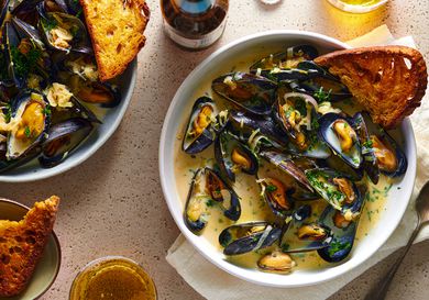 A bowl of moules mariniÃ¨res with a piece of bread in it.