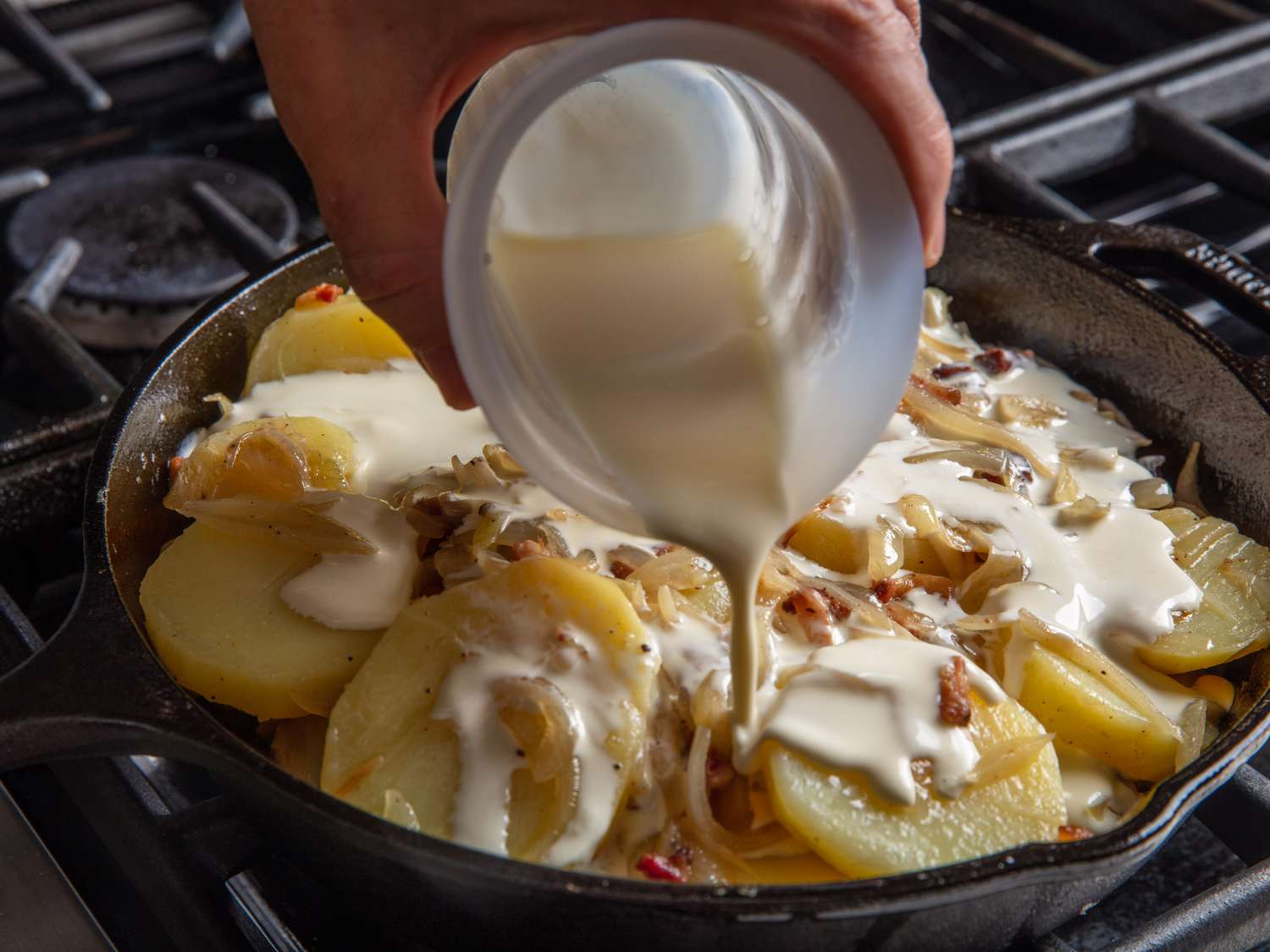 Heavy cream is poured into the potatoes and onions in the skillet.