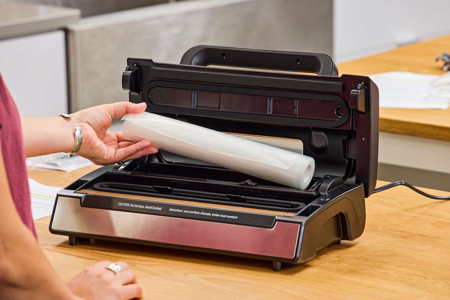 A person places a plastic bag roll into the Nesco VS-12 Deluxe Vacuum Sealer