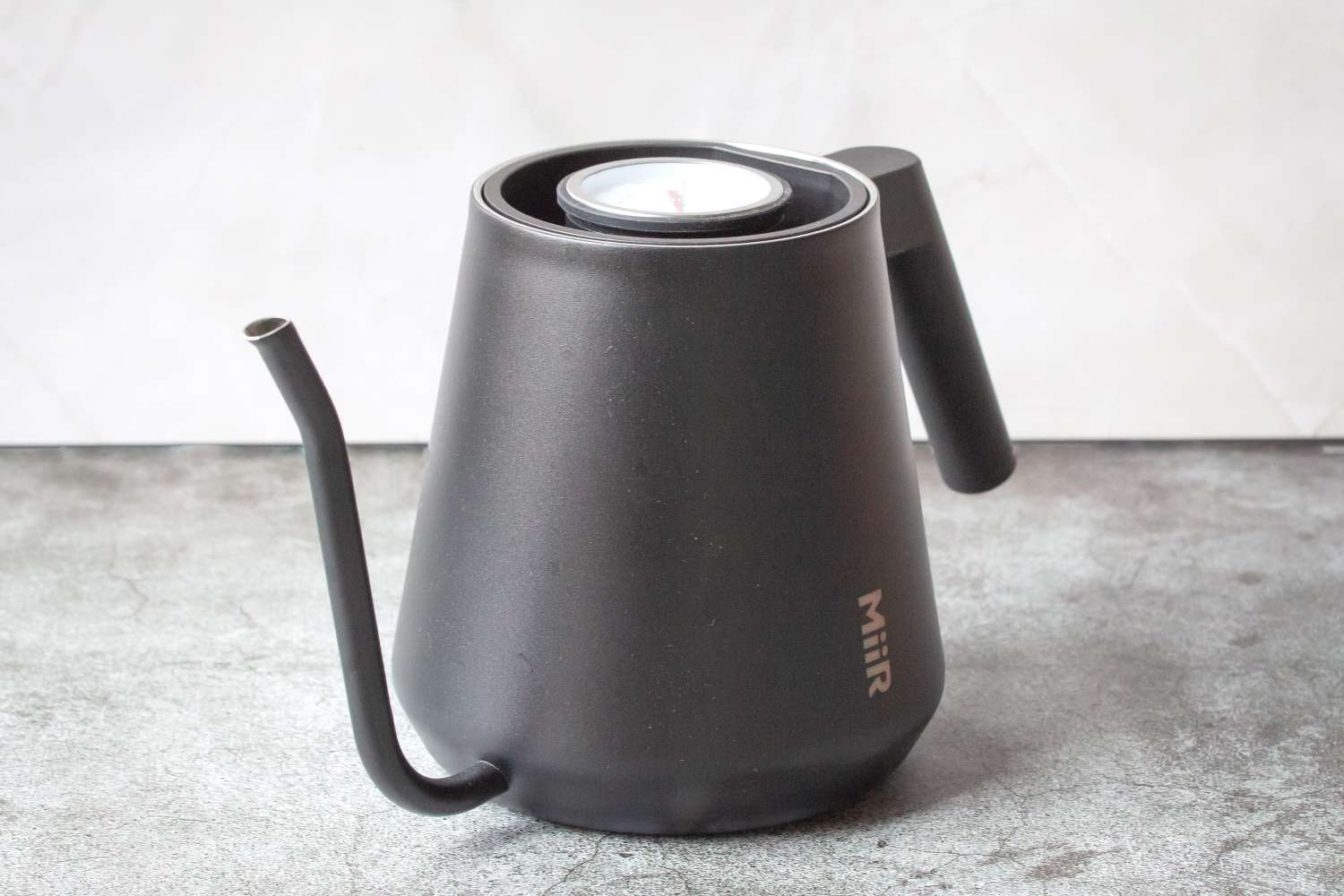 A metal kettle with a builtin thermometer on a textured surface