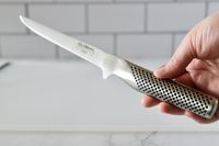 A person holding the handle of the Global boning knife.