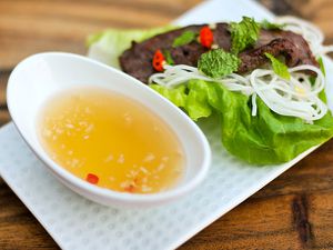 A dish of nuoc cham on a plate containing lettuce, vermicelli and a piece of grilled meat.